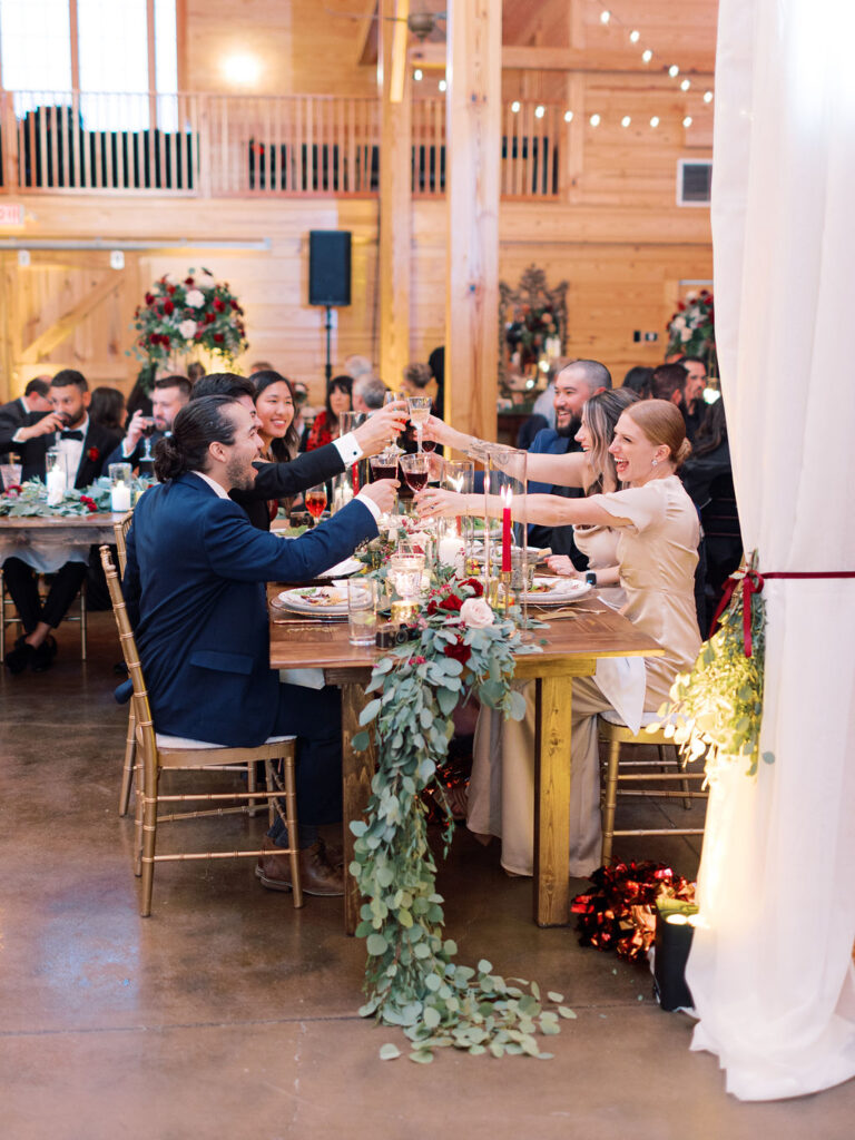 Wedding guests toasting while sitting at farm tables at The Middleburg Barn Virginia wedding venue
